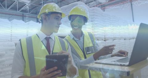 Warehouse team reviewing tablet and laptop, collaborating on logistics data in facility