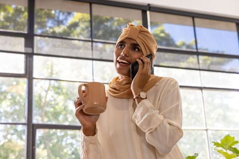 Smiling Professional Woman Talking on Phone with Coffee Mug in Office