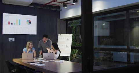 Three colleagues collaborating over sales analytics and charts in modern glass-walled boardroom