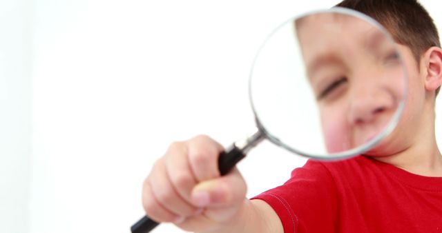 Happy caucasian preschool boy in red t-shirt, looking through magnifier on white background. Children, childhood, playing time and preschool activities, science and knowledge, unaltered.