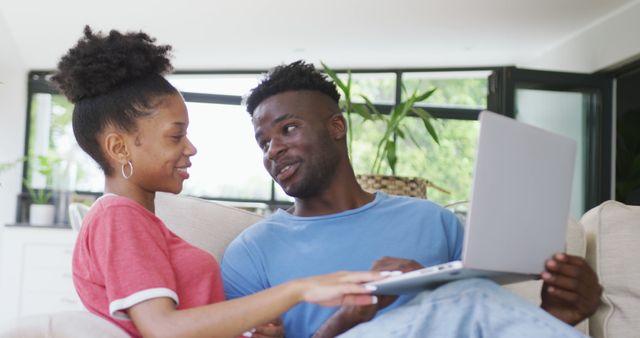 Image of happy african american couple sitting on sofa and using laptop. love, relationship, togetherness and spending time with technology at home.