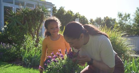 Mother and daughter smelling lavender in sunlit backyard garden