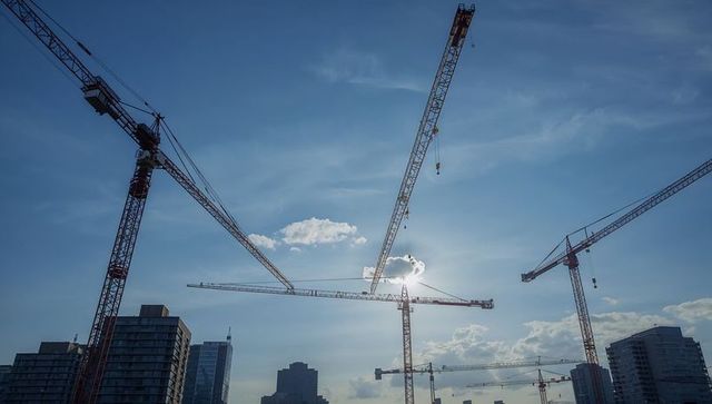 Crossing tower cranes over downtown skyline with sun glare and hoist cables, urban construction