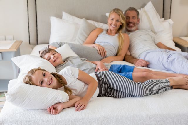 Portrait of smiling parents and kids relaxing on bed in bedroom at home