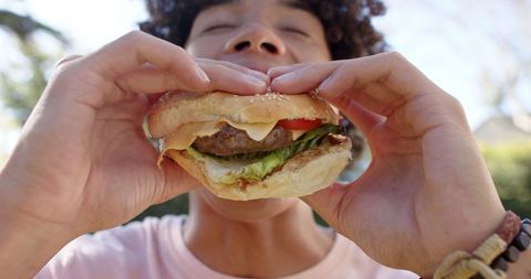 Person Enjoying Cheeseburger Outdoors in Sunny Park