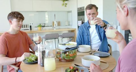Family raising glasses over healthy homemade meal in bright modern kitchen