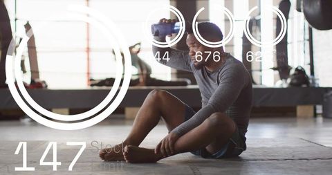 Cooling athlete sitting on gym mat holding water bottle with digital fitness readouts