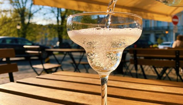 Sunlit sparkling drink pouring into coupe glass on wooden table at outdoor cafe