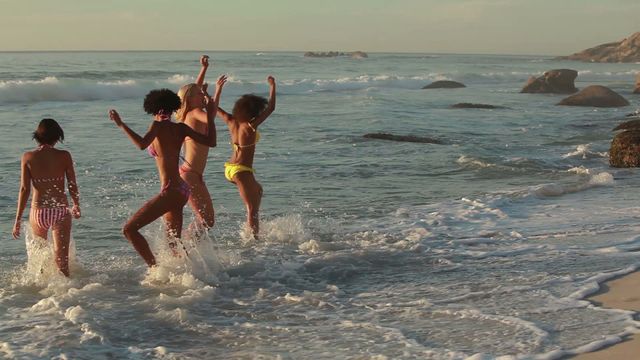 Group of young women enjoying splash in ocean waves during sunset. Perfect for themes related to summer vacations, beach activities, friendship, joy, and youthful fun.