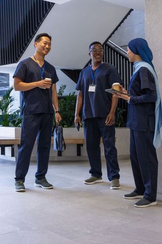 Diverse healthcare team in navy scrubs sharing coffee and discussing care in modern clinic lobby