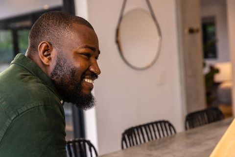 African american man smiling and leaning on kitchen counter in modern home interior