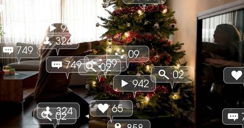 Kneeling woman decorating christmas tree with social media icons overlay, cozy living room