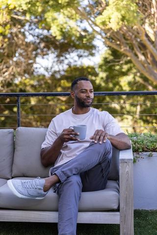 Mature african american man relaxing on patio sofa holding mug in sunny morning terrace