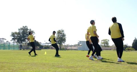 Diverse male team practicing field drills in yellow tops and black pants on sunny grass