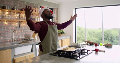 African American man wearing Santa hat baking cookies in rustic kitchen, celebrating joy