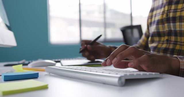 This image shows a businessman working at a modern office desk, typing on a keyboard and using various electronic devices. It can be used for business-related articles, remote work promotions, office environment illustrations, and technology advancements in workplace settings.