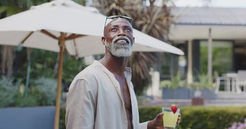Senior african american man relaxing on sunlit patio holding strawberry garnish drink