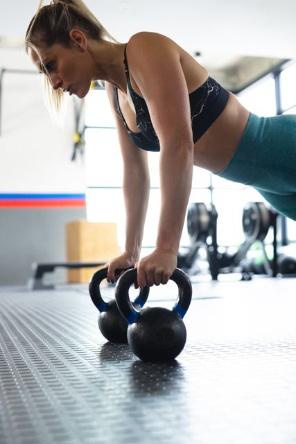 Fit woman performing press ups with weights in a gym, showcasing strength and determination. Ideal for promoting fitness, health, and active lifestyle concepts. Suitable for use in fitness blogs, workout guides, gym advertisements, and health-related articles.