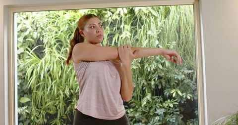 Woman stretching arm beside indoor vertical garden for home workout and wellness