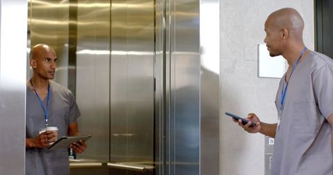African medical staff discussing in elevator while using tablet and smartphone