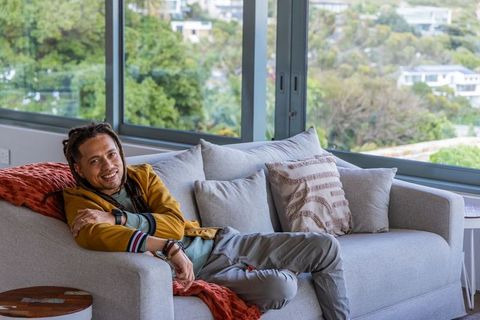 Relaxed man reclining on modern gray sofa by large windows with lush view and cozy throw