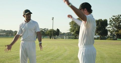 Diverse cricket teammates discussing strategy on sunny green field wearing white kit