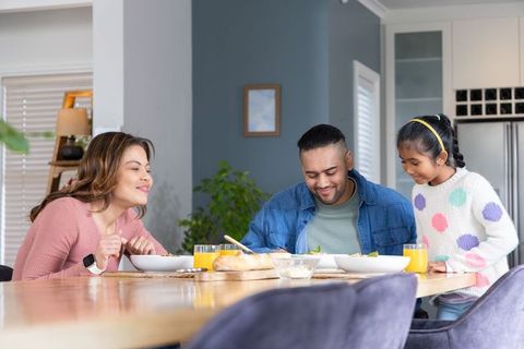 Multicultural family sharing cozy sunlit breakfast at wooden dining table with child
