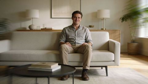 Smiling middle-aged man relaxing on beige sofa in sunlit modern living room