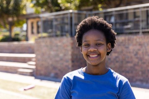 African-american teen girl smiling in blue t-shirt on school campus, sunny portrait