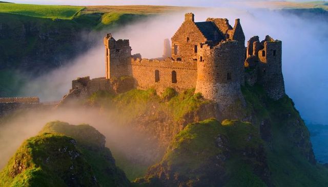 Sunlit ruined castle perched on misty coastal cliff at golden hour medieval fortress