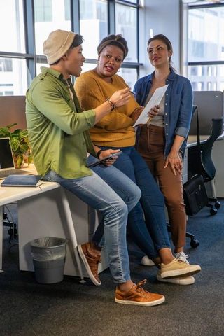 Diverse team collaborating around desk in modern office with tablet and printed notes
