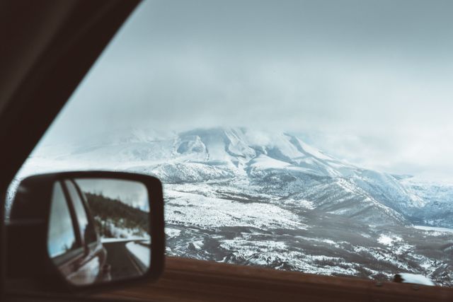 Viewing a snow-covered mountain landscape from a car mirror. Ideal for winter travel themes, road trip illustrations, or nature scenery backgrounds.
