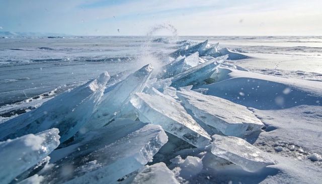 Glittering blue ice slabs forming jagged ridge along frozen shoreline under pale winter sky