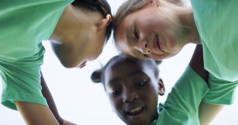 Huddling multiracial girls wearing matching green shirts forming team circle outdoors