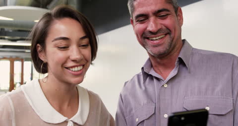 Colleagues Collaborating and Smiling Over Smartphone in Office