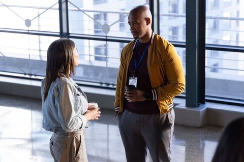 Diverse coworkers chatting in modern office atrium holding coffee and lanyards