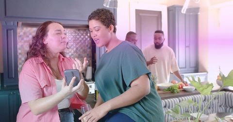 Friends sharing phone at kitchen island during cozy home gathering with cooking
