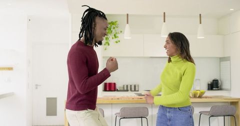 Young couple celebrating and dancing in bright modern minimalist open-plan kitchen