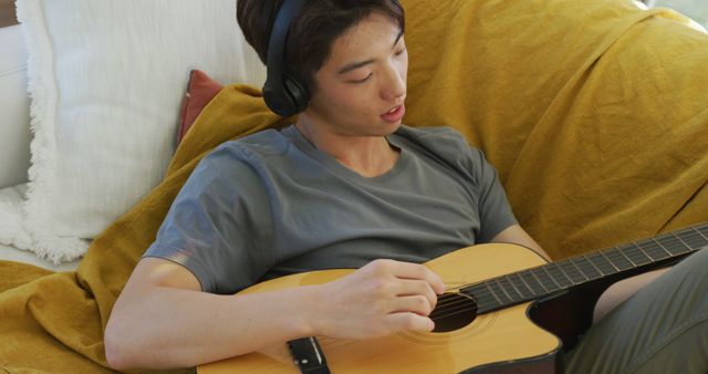 Asian boy wearing headphones playing guitar lying on bean bag at home. teenager lifestyle and living concept