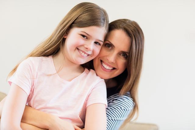 This heartwarming scene captures a loving mother and her daughter embracing and smiling warmly in a cozy living room. Perfect for conveying themes of family bonding, parental love, and happy home life. Ideal for use in parenting blogs, family-oriented advertisements, and social media posts celebrating family relationships.