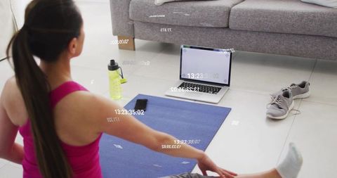 Home yoga stretching routine with laptop workout guide, water bottle and sneakers nearby