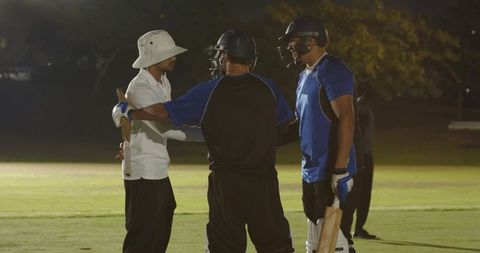 Diverse cricket teammates celebrating partnership, shaking umpire hand, walking off field at night