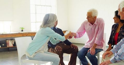 Older adults shaking hands during group meeting in bright sunlit community room