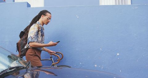 Man With Dreadlocks Wheeling Bicycle While Using Smartphone