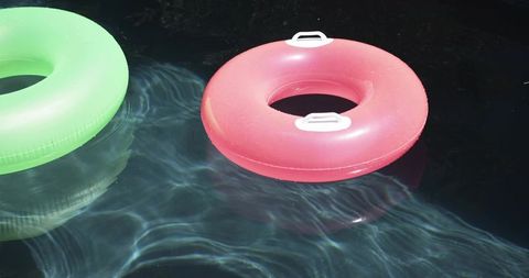 Pink inflatable swim ring with white handles floating on sunlit pool ripples