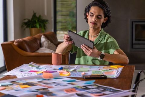 Asian man reviewing tablet and creative moodboard with sticky notes on home office desk