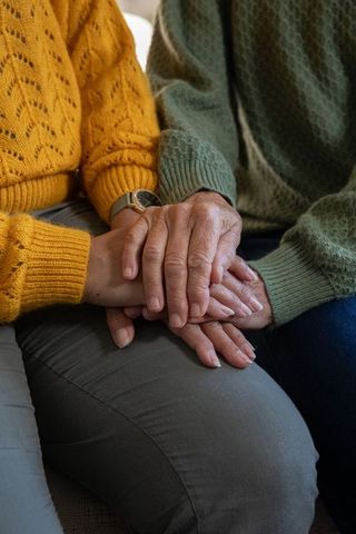 Senior women holding hands on couch, wearing knit sweaters and wristwatch, close-up