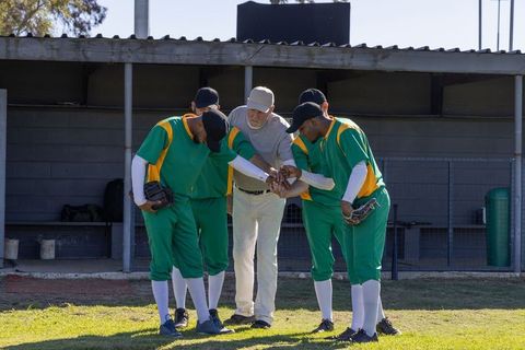 Senior coach leading huddle with african american baseball players wearing green uniforms