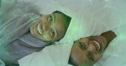 Mother and daughter lying on towels wearing spa robes while smiling with green ar skincare overlay