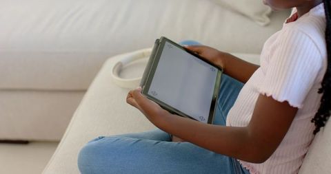 African-American Teen Sitting on Sofa Using Tablet for Learning and Relaxation